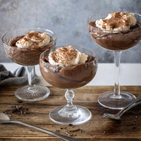 Three glass dishes filled with chocolate mousse and whipped cream on a wooden surface.