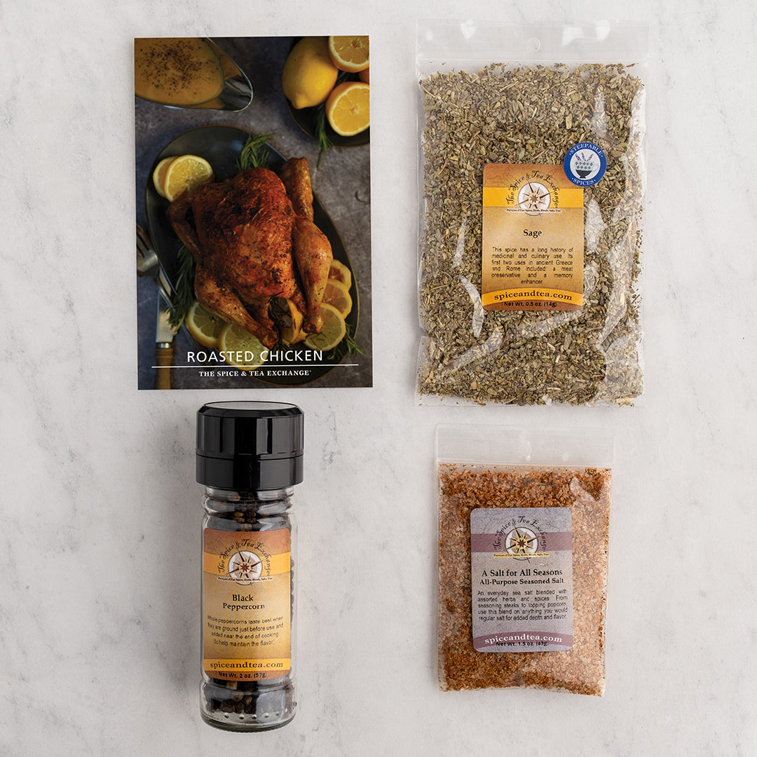 A flat-lay of a seasoning and recipe kit on a white marble background, including a recipe card for roasted chicken, a bag of seasoning, a bottle of sage, and a Black Peppercorn grinder.