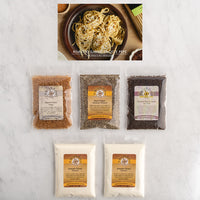 Five bags of gourmet spices and seasonings arranged on a white marble surface, with a top inset photo showing roasted garlic pasta.