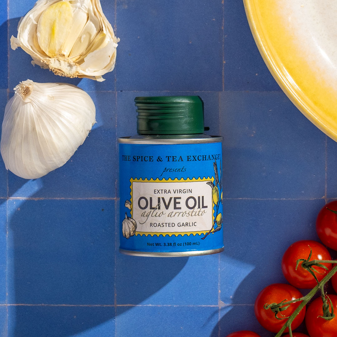 Can of Roasted Garlic Extra Virgin Olive Oil - Mini with garlic and tomatoes on a blue tiled background