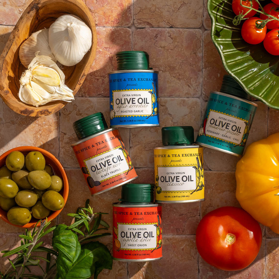 Assorted tins of olive oil with garlic, olives, and vegetables on a tiled surface