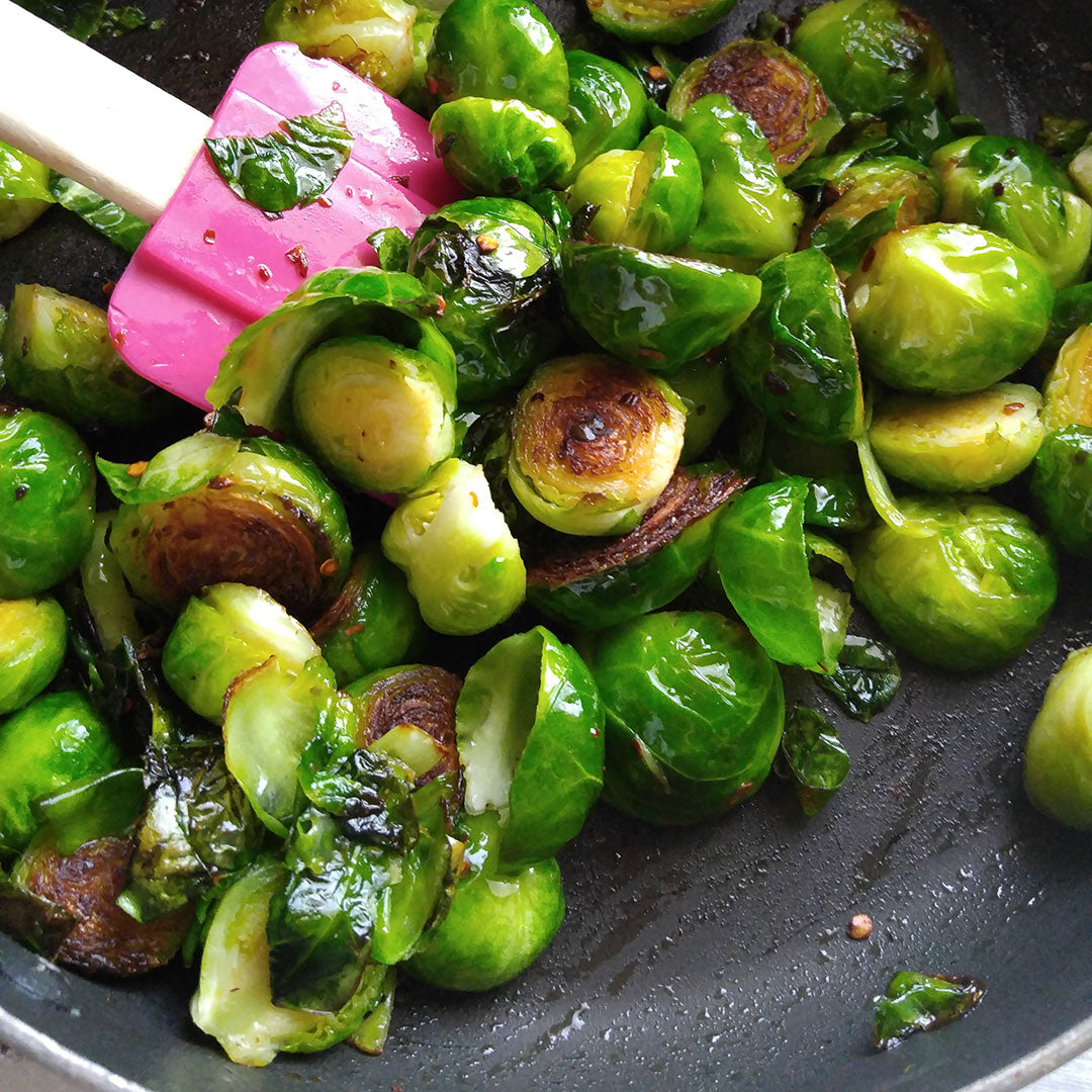 Sautéed Brussels sprouts with charred edges in a dark pan, with a pink spatula visible on the left side.
