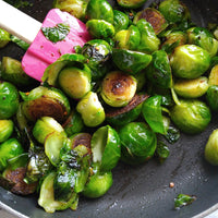 Sautéed Brussels sprouts with charred edges in a dark pan, with a pink spatula visible on the left side.