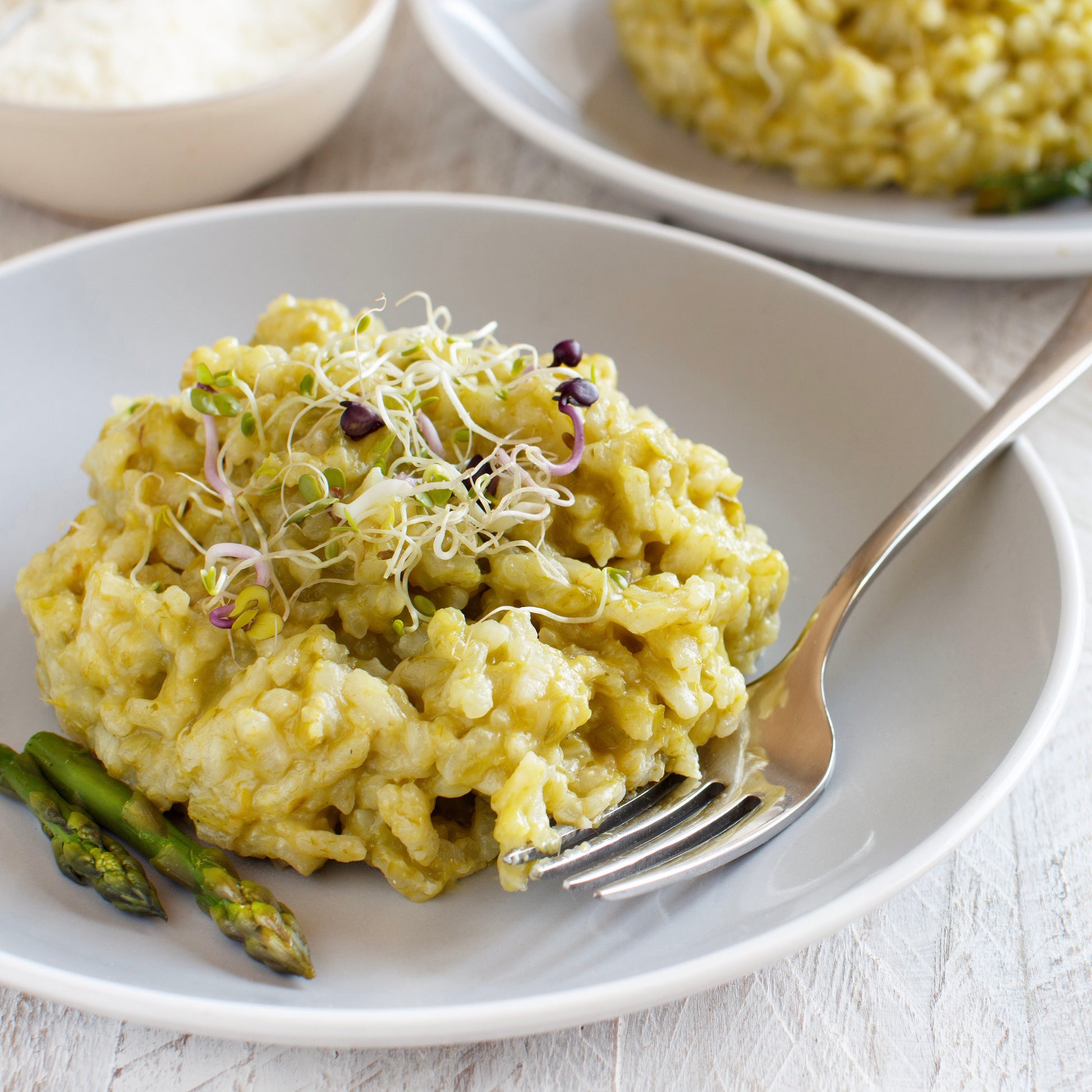 Green risotto with asparagus on a white plate with a fork