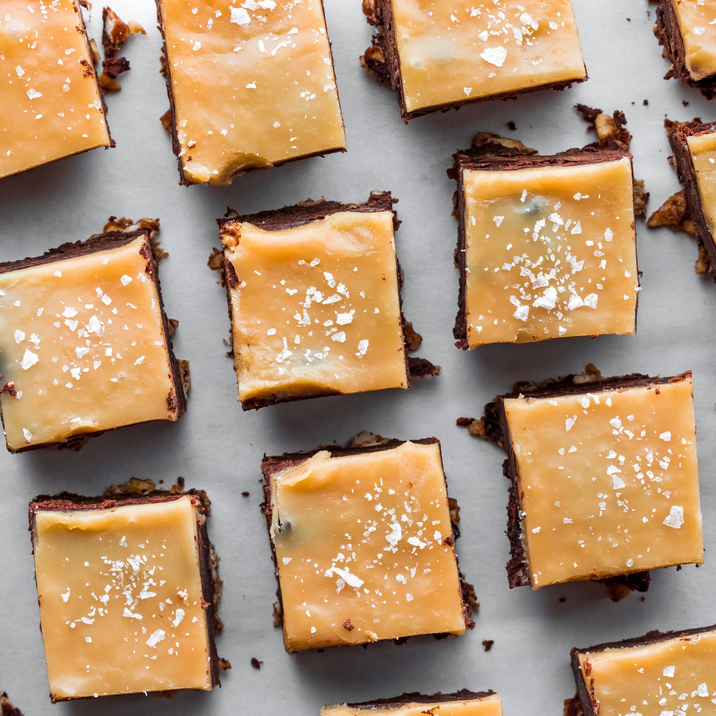 Square brownies with caramel topping and sea salt on a light gray background