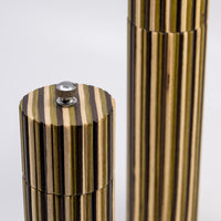 Close-up of a cylindrical product with a striped wood-grain pattern in black, brown, and tan, featuring a silver metal top knob on a light gray background.
