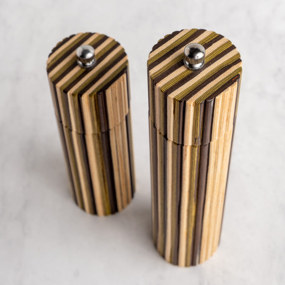 Two striped wooden cylindrical containers with silver metal screw tops, standing on a light marble-like surface.