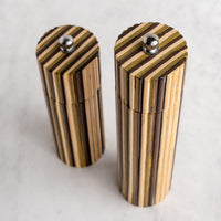 Two striped wooden cylindrical containers with silver metal screw tops, standing on a light marble-like surface.