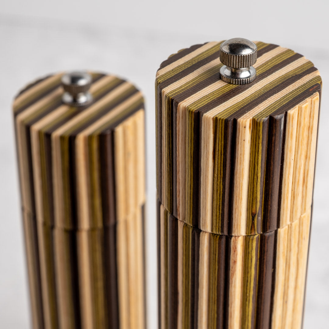 Close-up of two striped wooden cylindrical containers with metal screw tops, photographed on a light neutral background.
