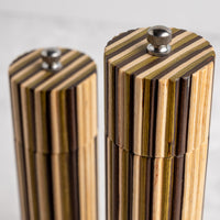 Close-up of two striped wooden cylindrical containers with metal screw tops, photographed on a light neutral background.
