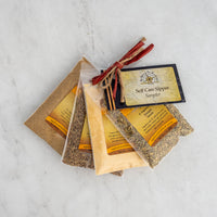 The Self Care Sipper Sampler features four clear pouches of coriander, cumin, fennel tea, and spices with yellow labels, tied with a red ribbon and tag—perfect for your daily ritual and elegantly arranged on marble.