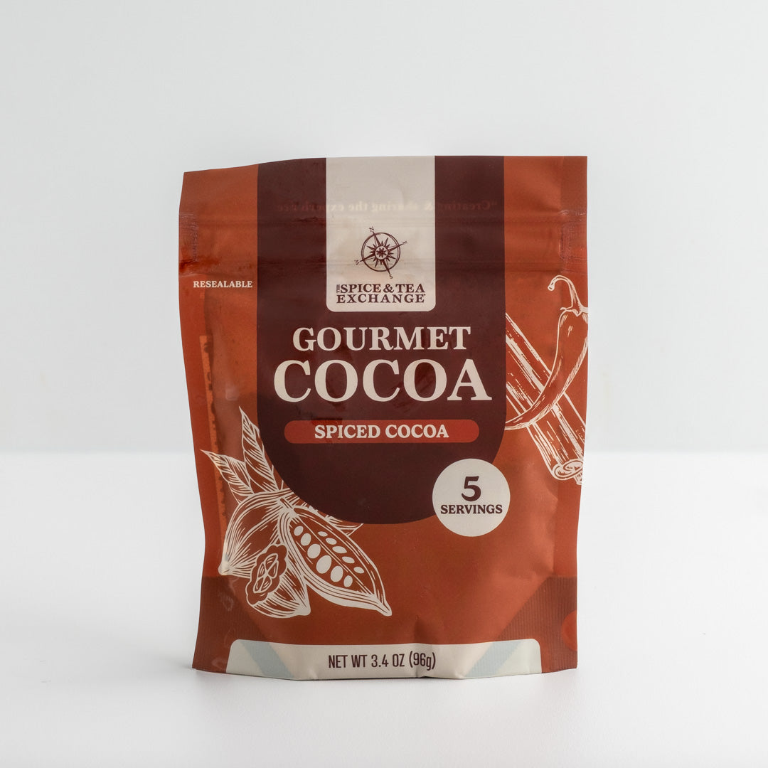 A resealable stand-up pouch of Spice & Tea Exchange Gourmet Cocoa Spiced Cocoa, shown on a clean white background. The packaging features a rich reddish-brown and dark brown color scheme with white text and illustrations of cocoa plants.