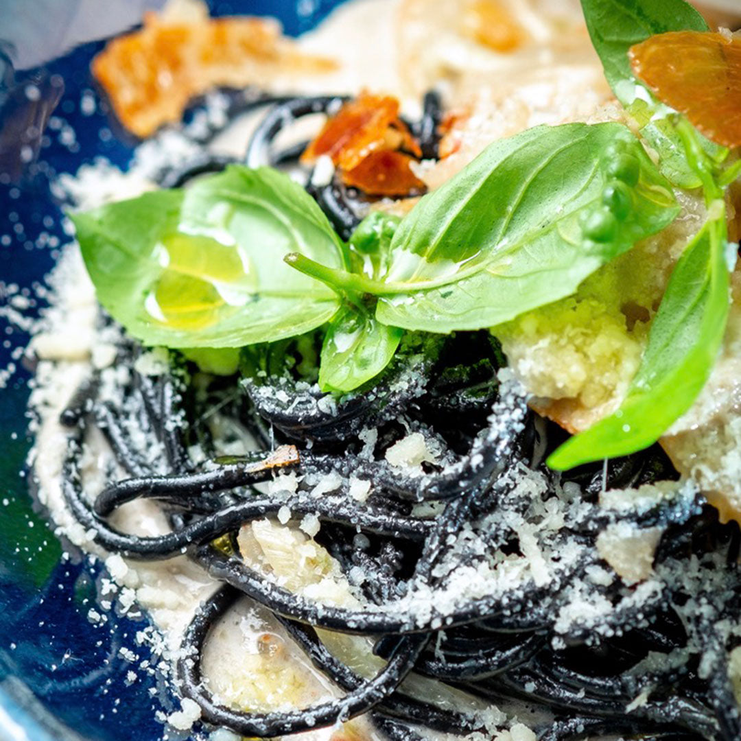 Black pasta dish with basil leaves on a blue plate