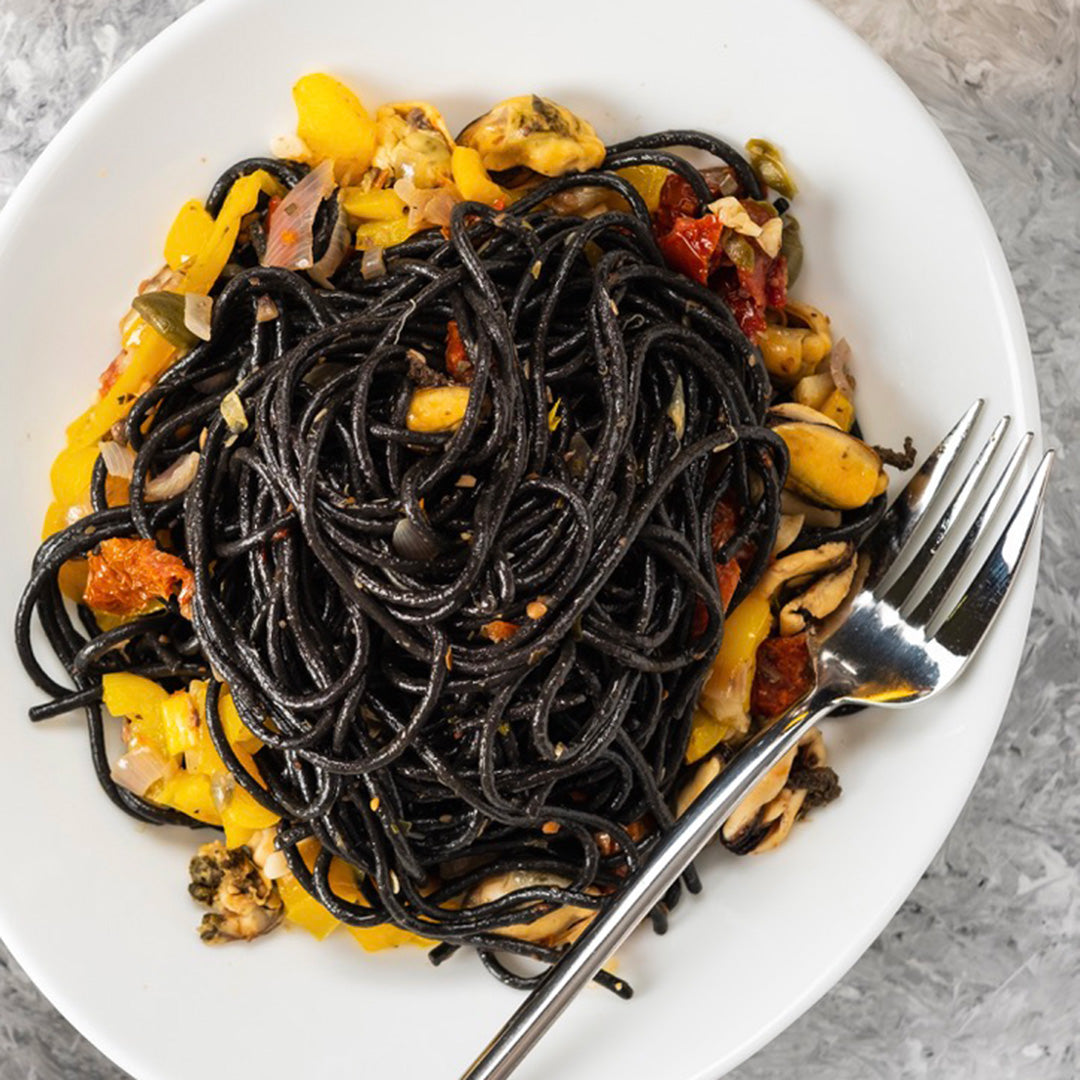 Black spaghetti pasta with a colorful topping on a white plate with a fork.