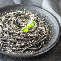 Black spaghetti on a dark plate with a basil leaf