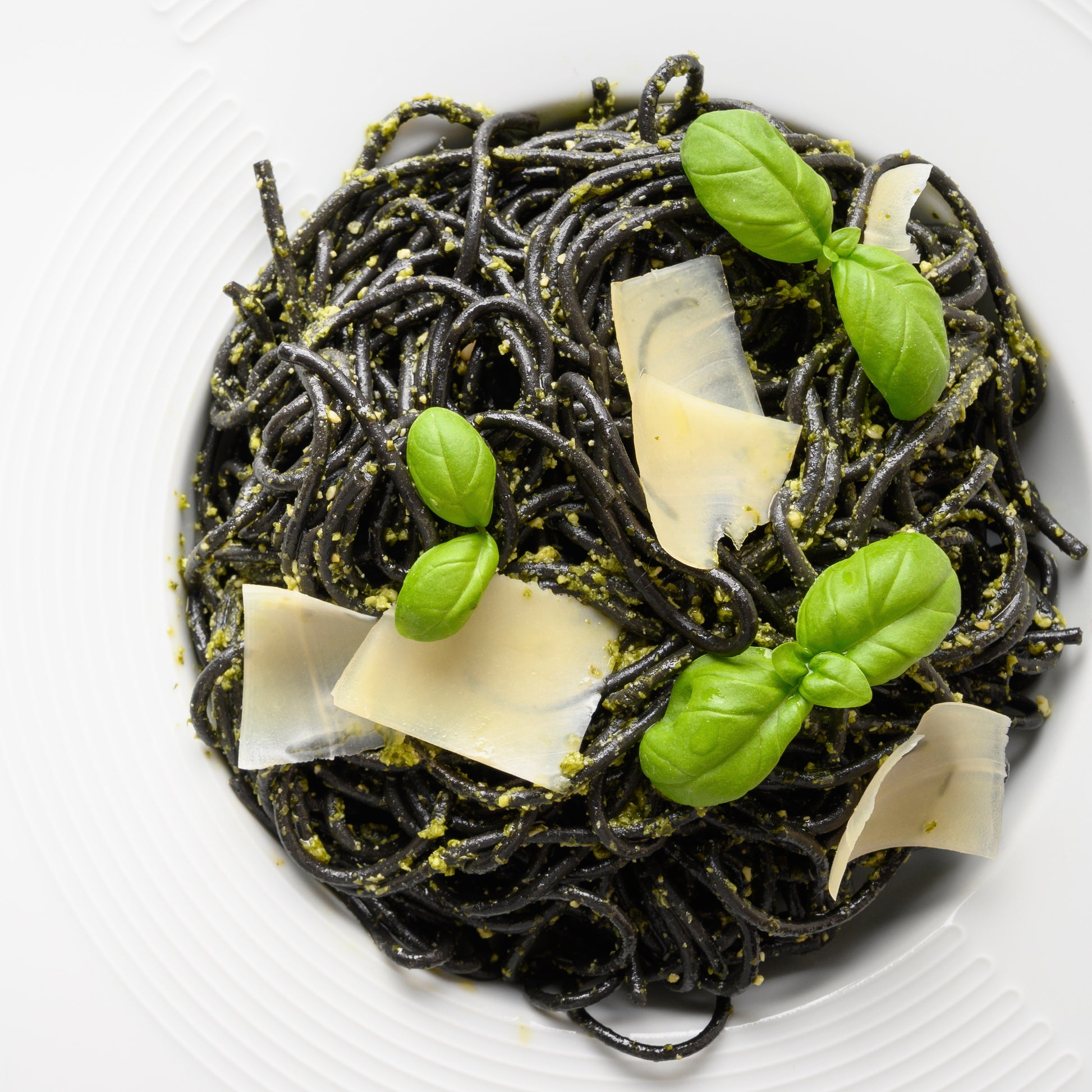 Black pasta dish with basil leaves and parmesan cheese on a white plate