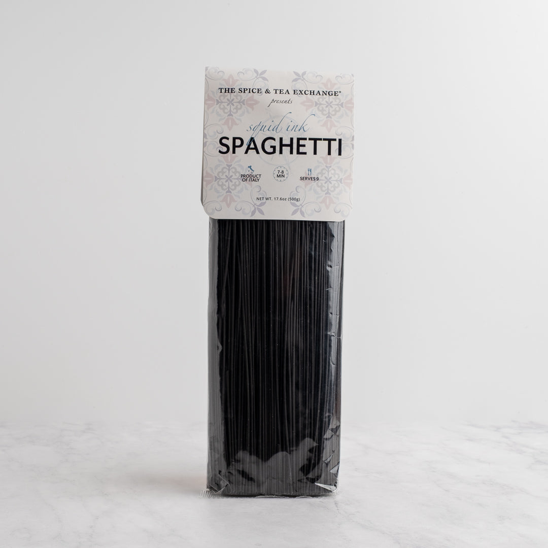 A package of black spaghetti pasta standing upright on a light gray surface with a white background. The paper label reads 'The Spice & Tea Exchange' and 'SQUID INK SPAGHETTI'.