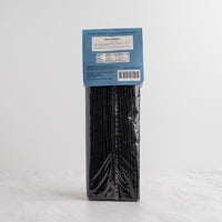 A package of black ink spaghetti from The Spice & Tea Exchange stands upright on a light marble surface against a white hexagonal tile wall. Back side.