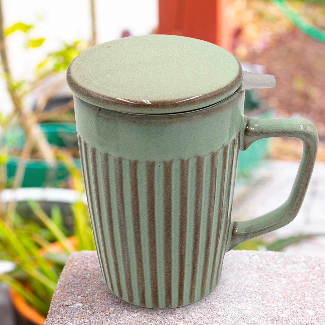 Green ceramic mug with a lid on a stone surface with blurred plants in the background