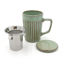 Green ceramic mug with striped pattern, metal tea infuser, and matching coaster on a white background