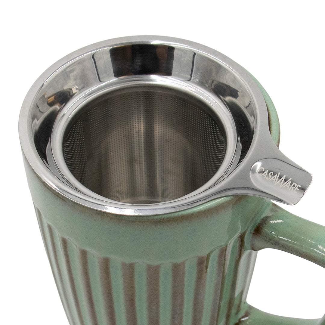Green mug with a metal tea infuser on a white background