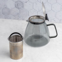 Stormy Glass Teapot with metal filter on a marble surface with hexagonal tile backsplash