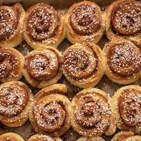 Row of cinnamon rolls with powdered sugar on a baking sheet