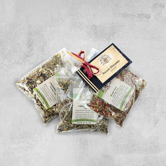 Three clear plastic bags of assorted teas from the Sweet Dreams Sampler are arranged on a grey surface, with a labeled card and ribbon attached.