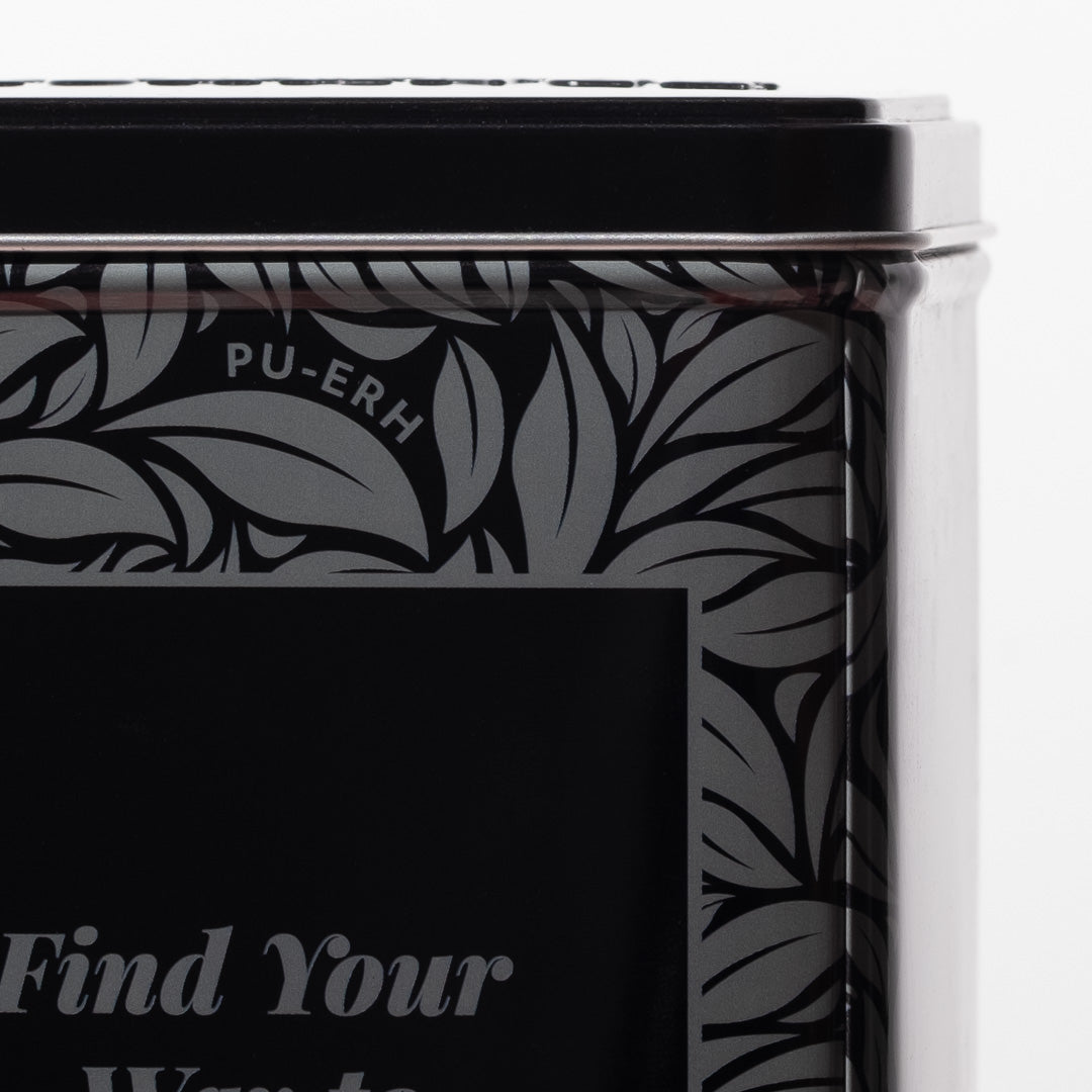 Tea canister with black leaf pattern and text on a white background zoomed in on corner