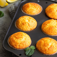 A close-up of six golden-brown muffins in a nonstick pan, garnished with fresh mint and a plaid cloth underneath, highlights the sweet citrus flavor of Tangerine Whipped Honey.