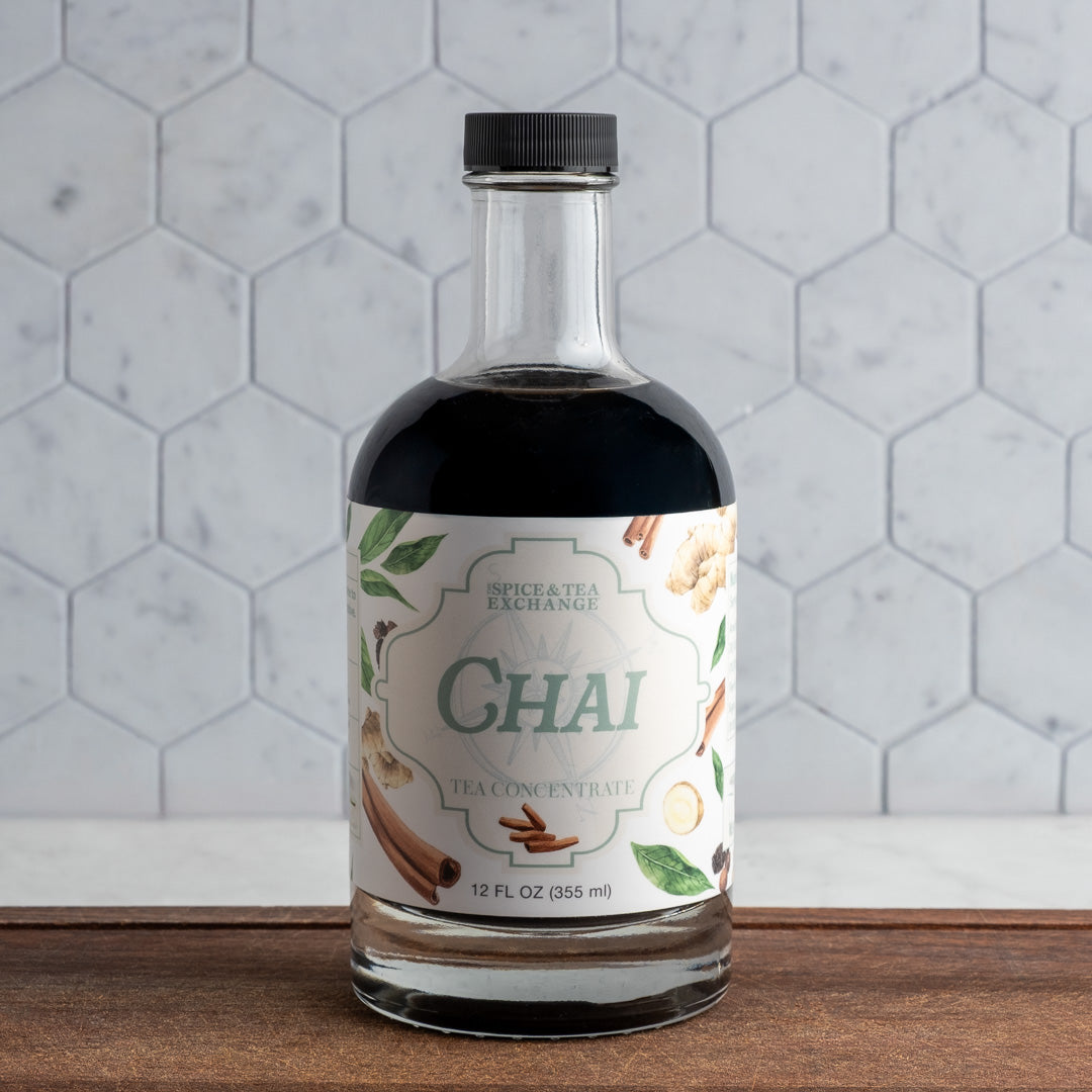 Bottle of Spice & Tea Exchange Chai tea concentrate on a wooden surface with a hexagonal tile background.