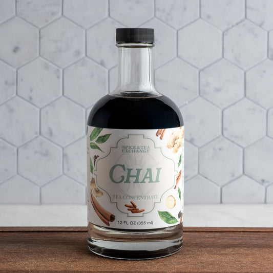 Bottle of Spice & Tea Exchange Chai tea concentrate on a wooden surface with a hexagonal tile background.