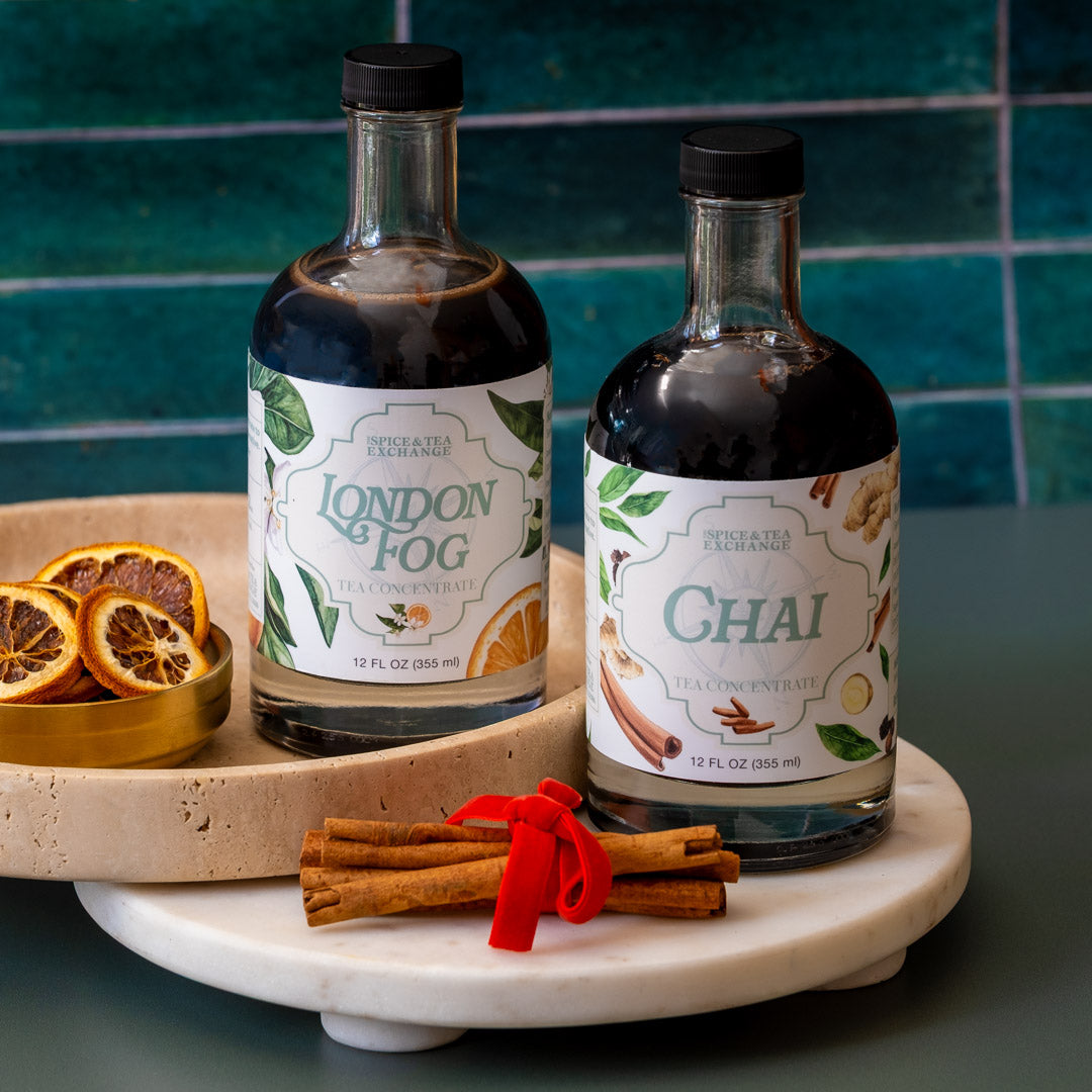 Two bottles of London Fog and Chai tea concentrates on a marble tray with decorative elements against a blue tiled wall.