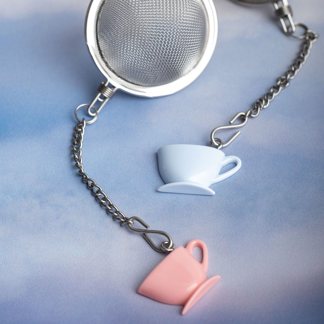 Tea infuser with chain featuring a blue teacup and pink saucer charm on a light blue background