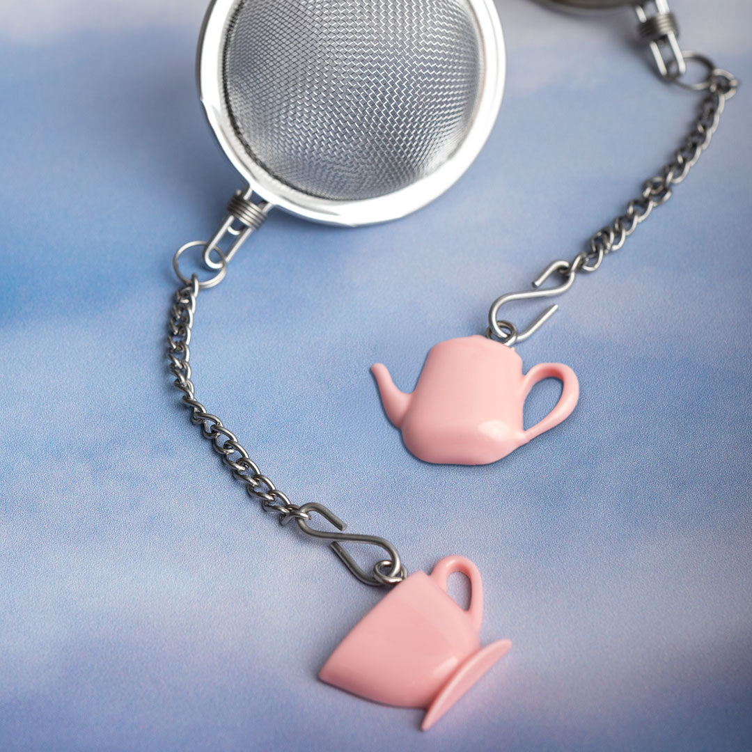Tea infuser with pink teacup and teapot charms on a blue background