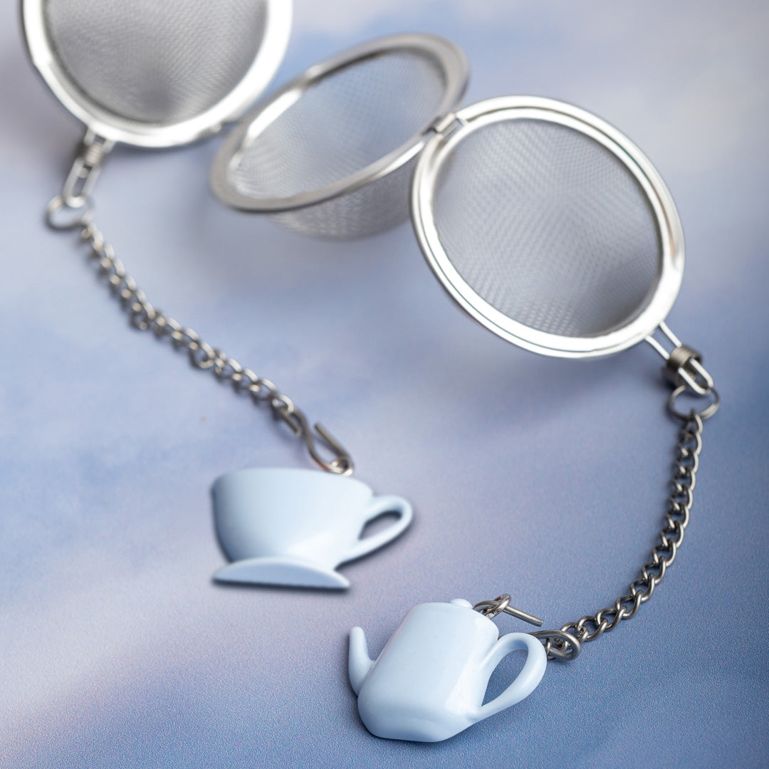 Tea infuser with teacup and teapot charm on a light blue background