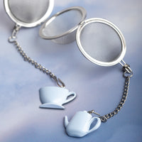 Tea infuser with teacup and teapot charm on a light blue background