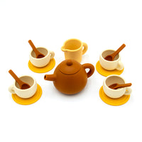 The Tiny Tea Party Toy Set features a brown teapot, small creamer, four cream cups with spoons, and yellow saucers—ideal for pretend play—beautifully arranged on a white background.