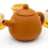 The Tiny Tea Party Toy Set features a brown teapot embossed with SPICE & TEA EXCHANGE and cream and yellow teacups—perfect for pretend play in any play kitchen, all set against a crisp white background.