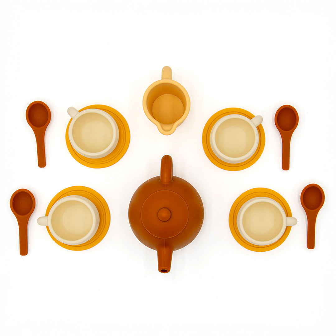 A top-down view of the Tiny Tea Party Toy Set shows six cups on saucers, six spoons, a teapot, and a creamer in brown, yellow, and cream shades—all neatly arranged for pretend play on a white background.