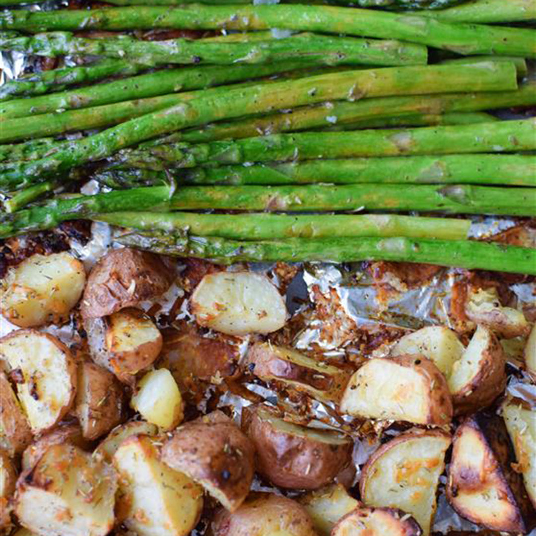 Roasted green asparagus and seasoned red potatoes on a foil-lined baking sheet.