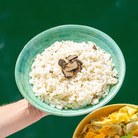 Green bowl of rice with mushrooms held by a hand against a green background