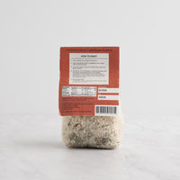 A package of Truffle Risotto rice from The Spice & Tea Exchange, featuring a white paper label with elegant gray patterns and a clear lower section showing the risotto grains inside, set against a clean white background. Back side.