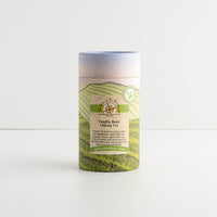 A cylindrical paperboard canister of Vanilla Bean Oolong Tea, featuring a green and beige landscape illustration and a light blue lid, set against a plain white background.