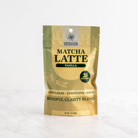 A stand-up pouch of Vanilla Matcha Latte on a light marble surface against a white background.