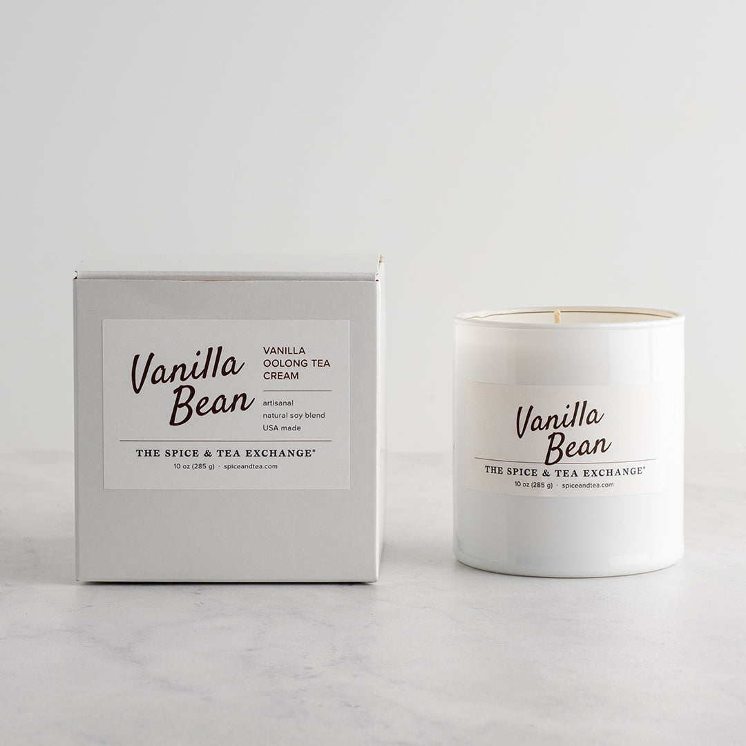 A white glass candle jar labeled 'Vanilla Bean' by The Spice & Tea Exchange, on a white background next to candle box.