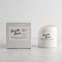A white glass candle jar labeled 'Vanilla Bean' by The Spice & Tea Exchange, on a white background next to candle box.