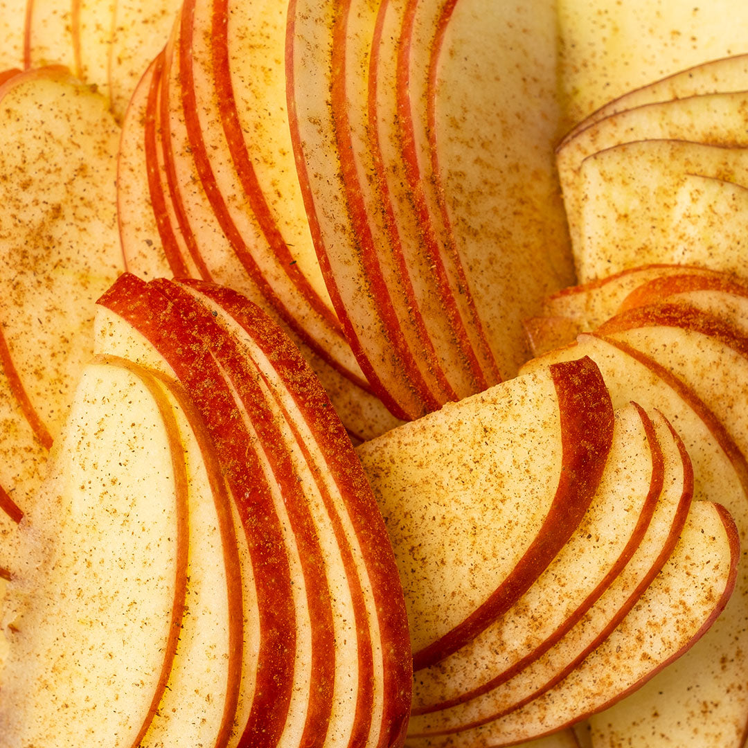 Close-up of thinly sliced red apples arranged in overlapping layers, dusted with cinnamon on a warm golden background.