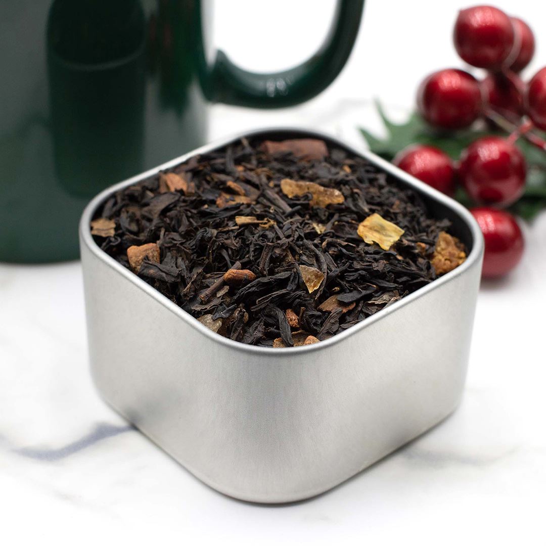 Warm Bread Pudding Tea in sq tin - green mug and cranberries in background