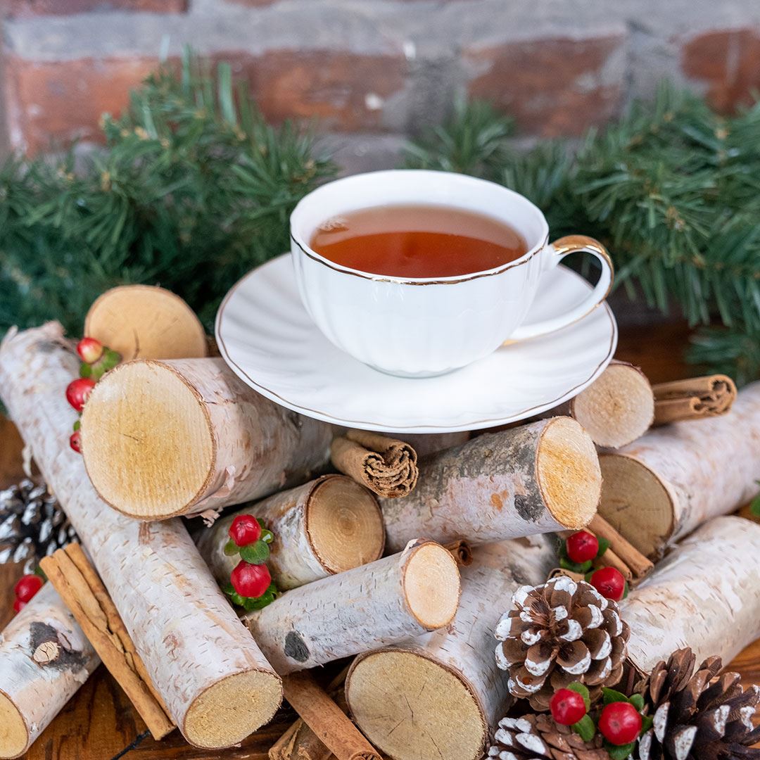 Warm Bread Pudding Tea in white mug on top of firewood in front of pine and brick wall
